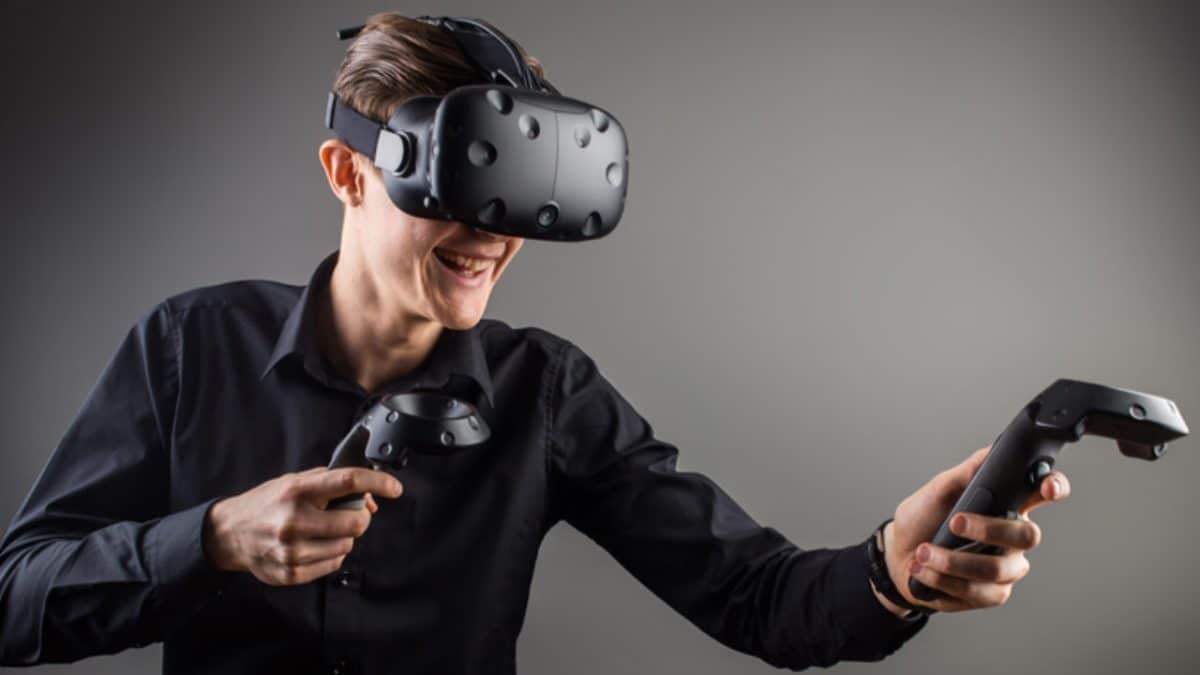 Un hombre se para frente a un fondo gris con un auricular VR y controladores encendidos.